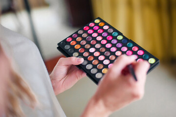 make-up artist holds a palette with multi-colored eyeshadows in his hands and picks them up on a brush