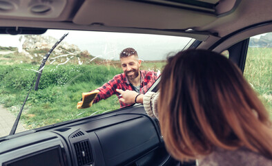 Man smiling cleaning van windshield with cloth while woman pointing stain