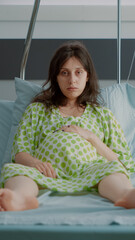 Portrait of pregnant person sitting in hospital ward bed with monitor preparing for child delivery...