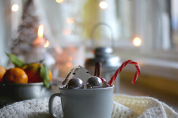 Silver bowl filled with fresh tangerines, various Christmas decorations, lit candles and soft blanket. Hygge at home. Selective focus.