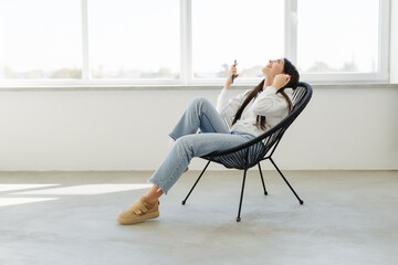 Beautiful woman use mobile phone with win gesture while sitting in armchair at home