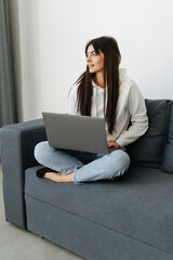 Happy woman using laptop sitting on cosy sofa
