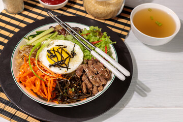 Korean cuisine, pibimpap with beef and vegetables. Close-up, hard shadows, horizontal with space