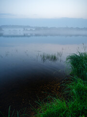 misty morning by the lake with calm water, fog and reflections of trees in mirror