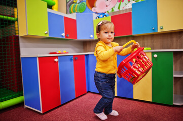 Cute baby girl playing in indoor play center. Kindergarten or preschool play room. Holds a basket...