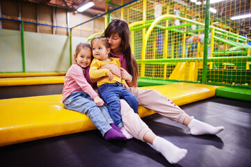 Mother with two daughters sitting on a trampoline in indoor play center.