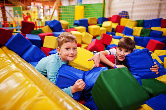 Two brothers lying on pool with colored foam cubes in indoor play center.