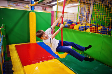 Smiling boy swinging on a rope at indoor playground.