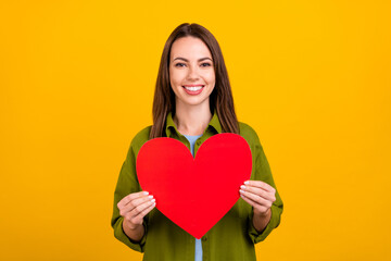 Photo of adorable pretty young woman dressed green shirt smiling holding big red heart isolated yellow color background
