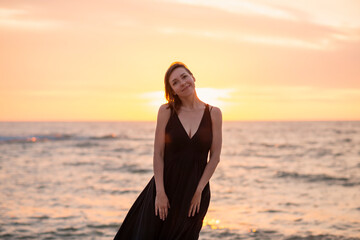 Fototapeta premium Beautiful woman stands in a dress near the sea at sunset