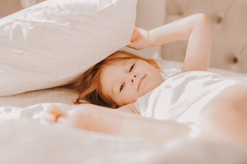 Cute toddler girl lies in bed with white linen.