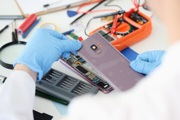 Master opening back cover of mobile phone in workshop closeup