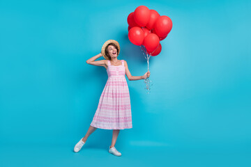 Full body photo of sweet young lady hold balloons look empty space wear hat long sarafan sneakers isolated on blue background