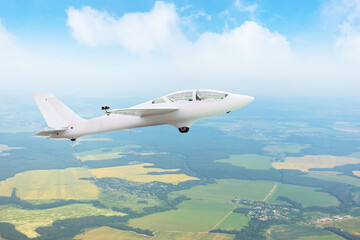 Glider flying high in the sky over fields and forests, aerial view.