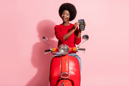 Portrait of attractive cheerful girl riding moped using terminal paypass service isolated over pink pastel color background