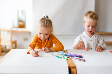 Funny kids Toddlers draw together with felt-tip pens on paper at the table, Montessori and...