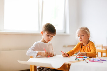 Funny kids Toddlers draw together with felt-tip pens on paper at the table, Montessori and creativity, creative development and activities in kindergarten. Boy and girl painting together