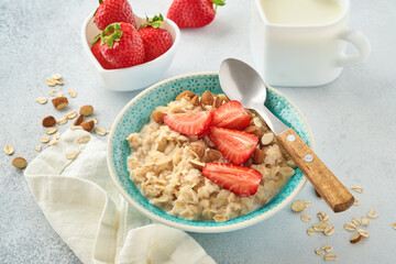 Oatmeal porridge with strawberry slices, nuts almonds and honey in blue bowl on grey table. Healthy eating, dieting, vegetarian food concept. Place for text