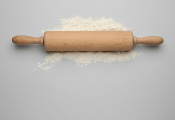 Wooden rolling pin and flour on light grey background, top view. Space for text