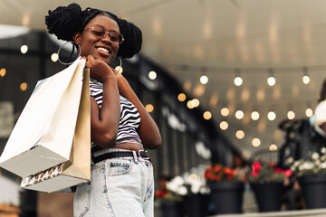 Attractive happy African American young woman shopping on Black Friday shopping mall with packages,...