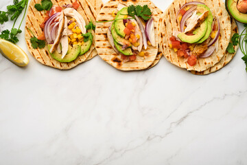 Mexican tacos with grilled chicken, avocado, corn kernels, tomato, onion, cilantro and salsa at white stone table. Traditional Mexican and Latin american street food. Top view.