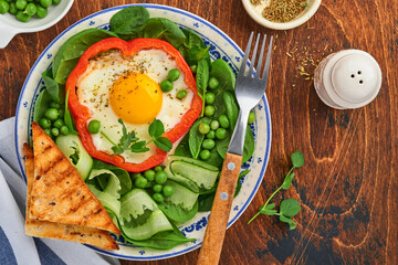 Red bell peppers stuffed with eggs, spinach leaves, green peas and microgreens on a breakfast plate on old wooden table background. Top view.