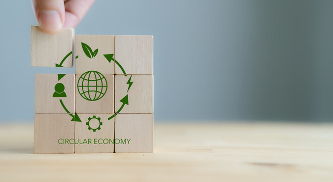 Circular economy concept, recycle, environment, reuse, manufacturing, waste, consumer, resource. Sustainable development. Hand put wooden cubes; the symbols of circular economy on grey background.