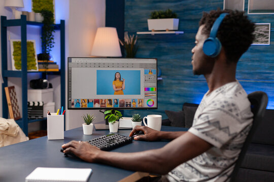 African american editor with headset doing retouching on creative photos. Photographer working on computer editing pictures using professional post production software. Digital photography on screen