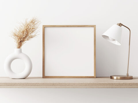 Empty square frame mockup in warm neutral minimalist interior with dried pampas grass, trendy vase and brass desk lamp on wooden beige brown shelf on white wall background. Illustration, 3d rendering