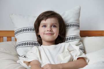 Portrait smiling cute male kid relaxing on comfortable pillow having positive emotion. Closeup face...