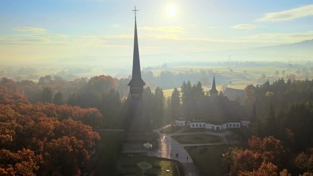 Aerial drone view of the Peri-Sapanta Monastery at sunrise, Romania. Main church and a building, visitors, yellowing forest around