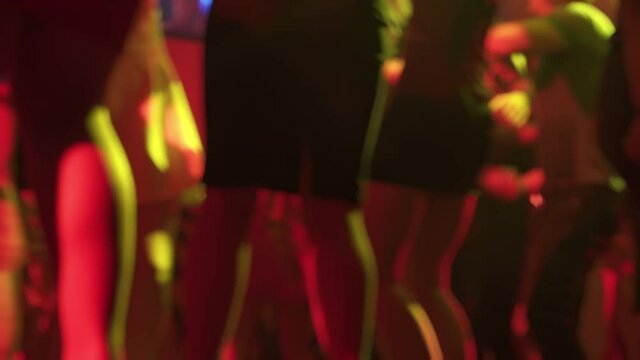Young ladies in short sexy dresses are spending time at night club dancing in the crowd. Back defocused view of caucasian women moving to the rhythm at the discotheque. Females are relaxing at a party