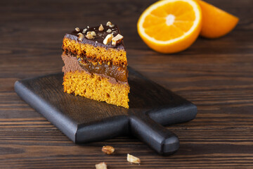 Piece of pumpkin pie with orange, chocolate and nuts on a wooden board. Sugar, gluten and lactose free and vegan.