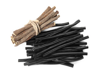Tasty black candies and dried sticks of liquorice root on white background, top view