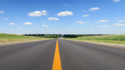 New asphalt pavement on the background of green fields to the horizon. A straight highway with a yellow flat strip on the background of a rural landscape