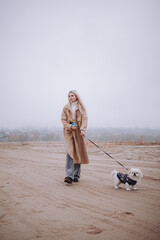 a girl on an autumn beach walks with a Pekingese dog, a foggy morning