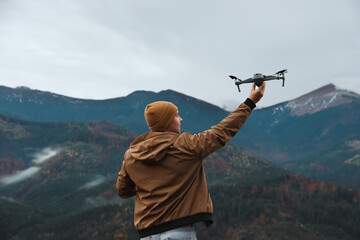 Young man with modern drone in mountains, back view