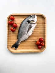 Raw dorado fish on the wooden plate with cherry tomatoes on white background. Top view. Cooking fish.