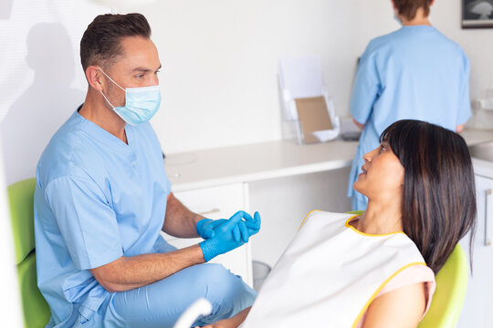 Caucasian male dentist wearing face mask talking to female patient at modern dental clinic