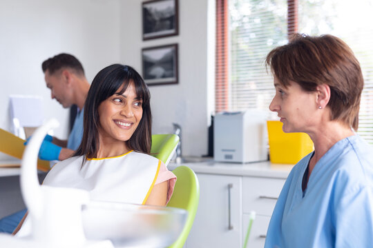 Caucasian female dental nurse talking to smiling female patient at modern dental clinic