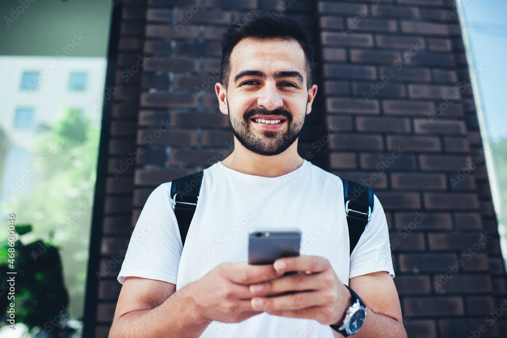 Poster half length portrait of glad travel blogger in casual wear smiling at camera while messaging in netw
