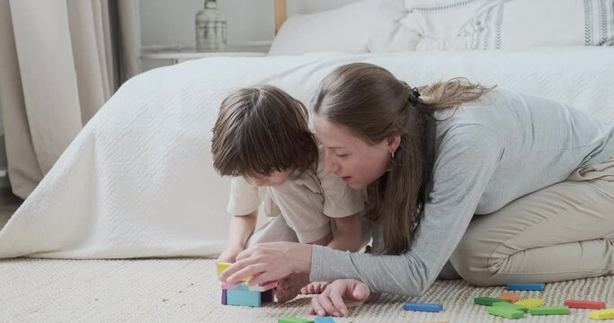 Confident family mom and son building multicolored bricks playing together enjoying weekend at home. Smiling kid boy neatly use constructor block cubes with mother having happy childhood motherhood