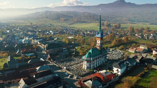 Aerial drone view of The Merry Cemetery in Sapanta, Romania. Church and multiple tombstones, visitors, residential buildings, yellowing trees