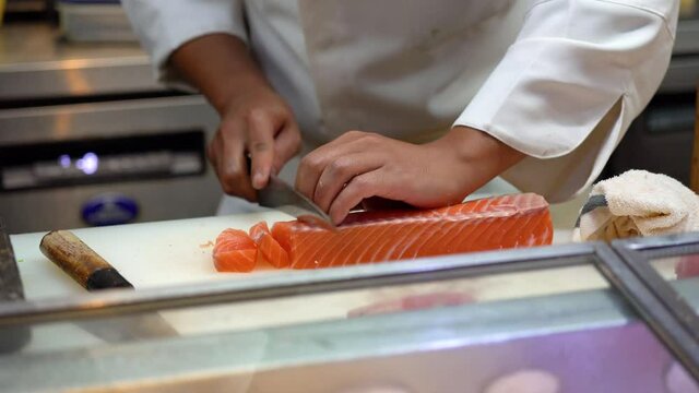 A master chef is using very sharp knife to cutting or slicing a big piece of salmon meat on the cutting board. Expertise cooking action 4k footage, Close-up and selective focus.