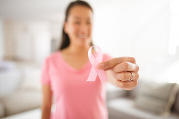Asian woman in pink tshirt showing breast cancer awareness pink ribbon at home