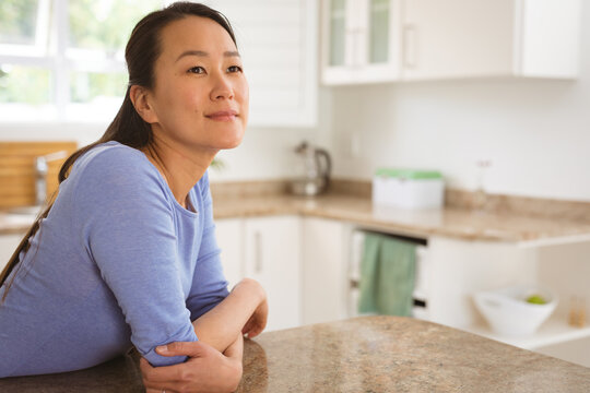 Portrait of happy asian woman sitting at table in kitchen