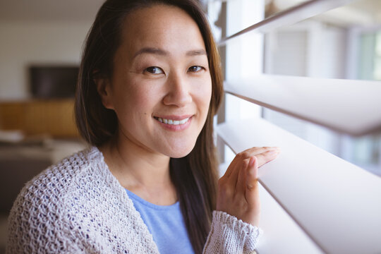 Portrait of happy asian woman standing at window, looking outside