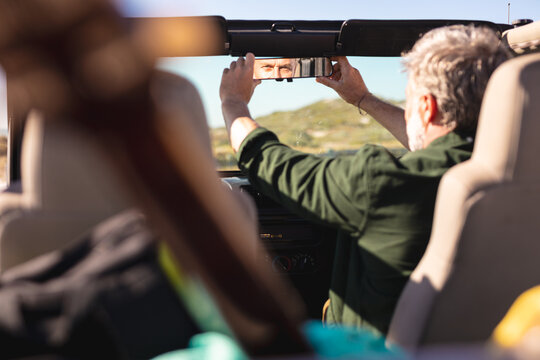 Caucasian man adjusting rearview mirror in car at seaside