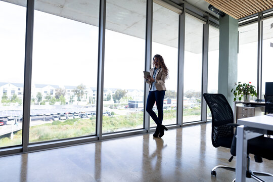 Creative businesswoman using digital tablet while leaning on window in office