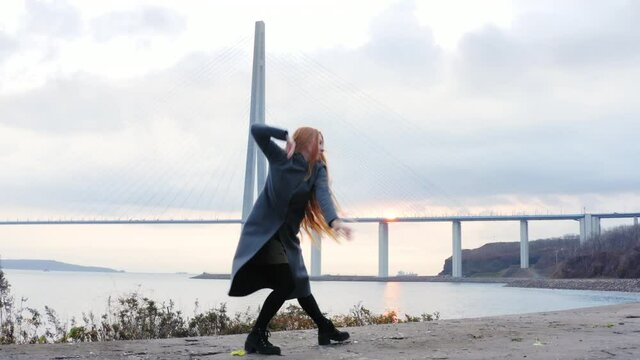 Aerial zooming out view of a woman with long hair dancing on the wall of the old fortifications on the island Russky. The cable-stayed Russian bridge in Vladivostok on the background